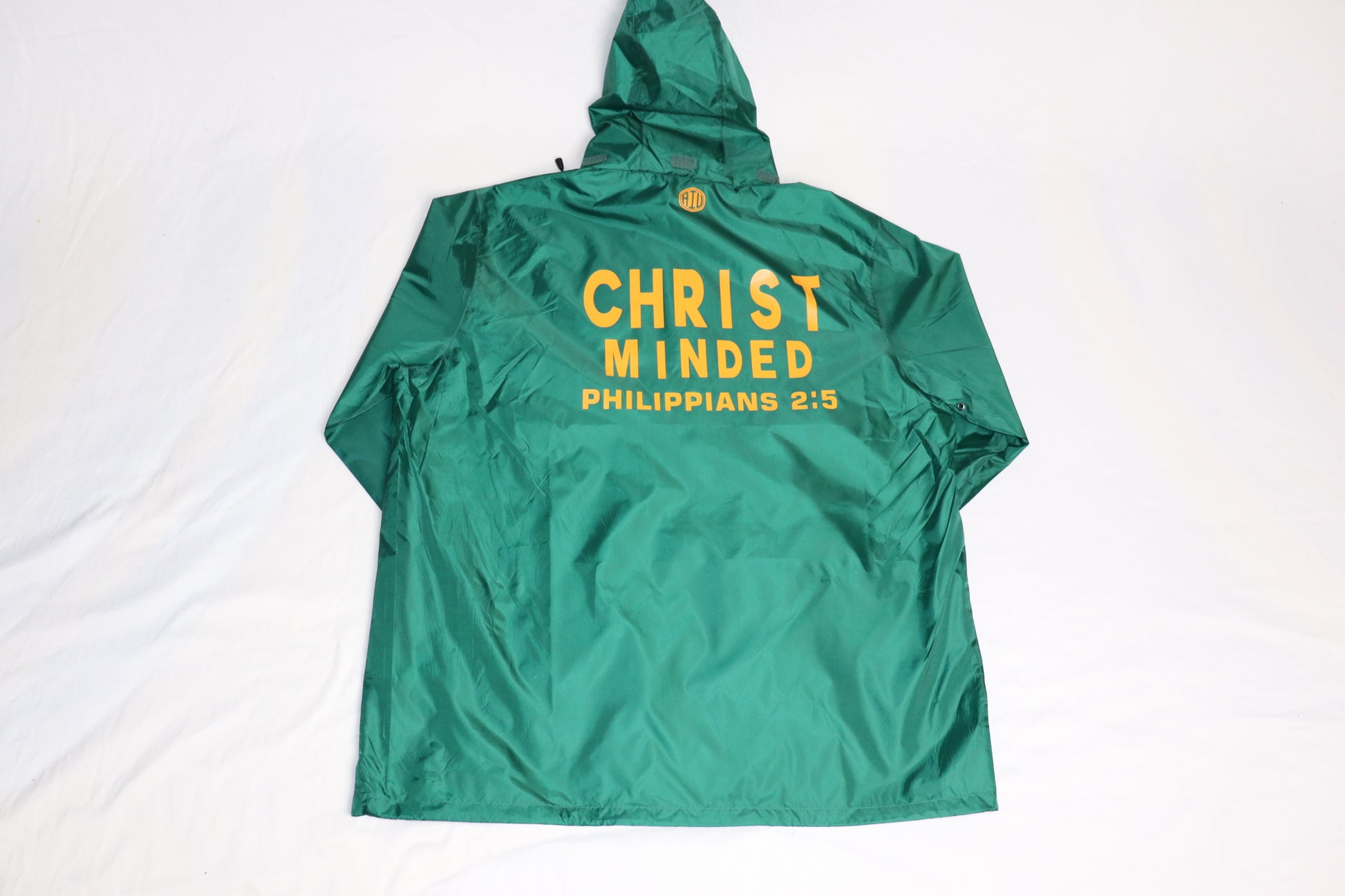 Back view of green Christian zip-up hooded jacket with yellow text reading “CHRIST MINDED PHILIPPIANS 2:5” across the back
