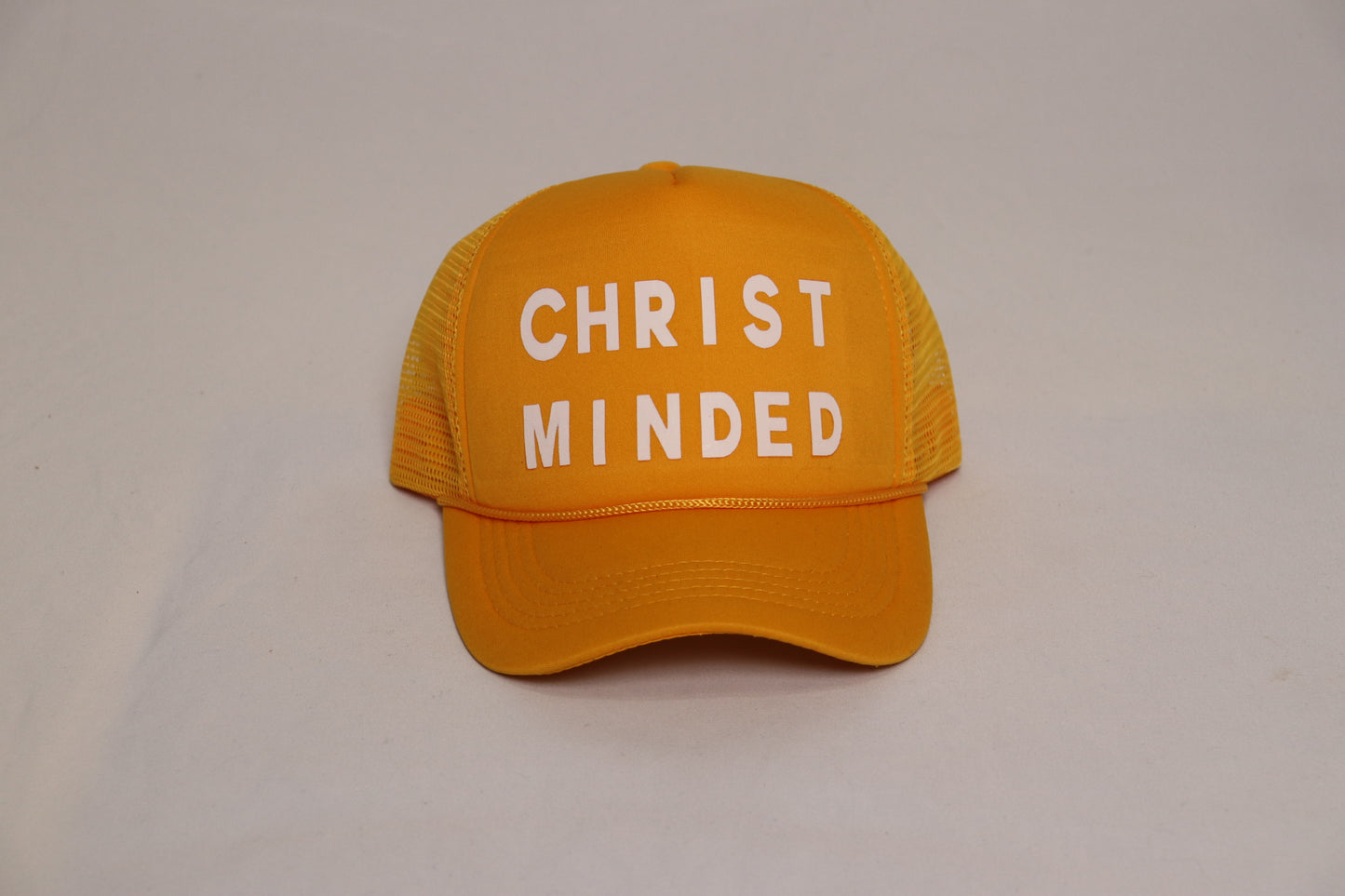 Christ Minded golden yellow faith-based trucker hat with bold white lettering on the front mesh cap.