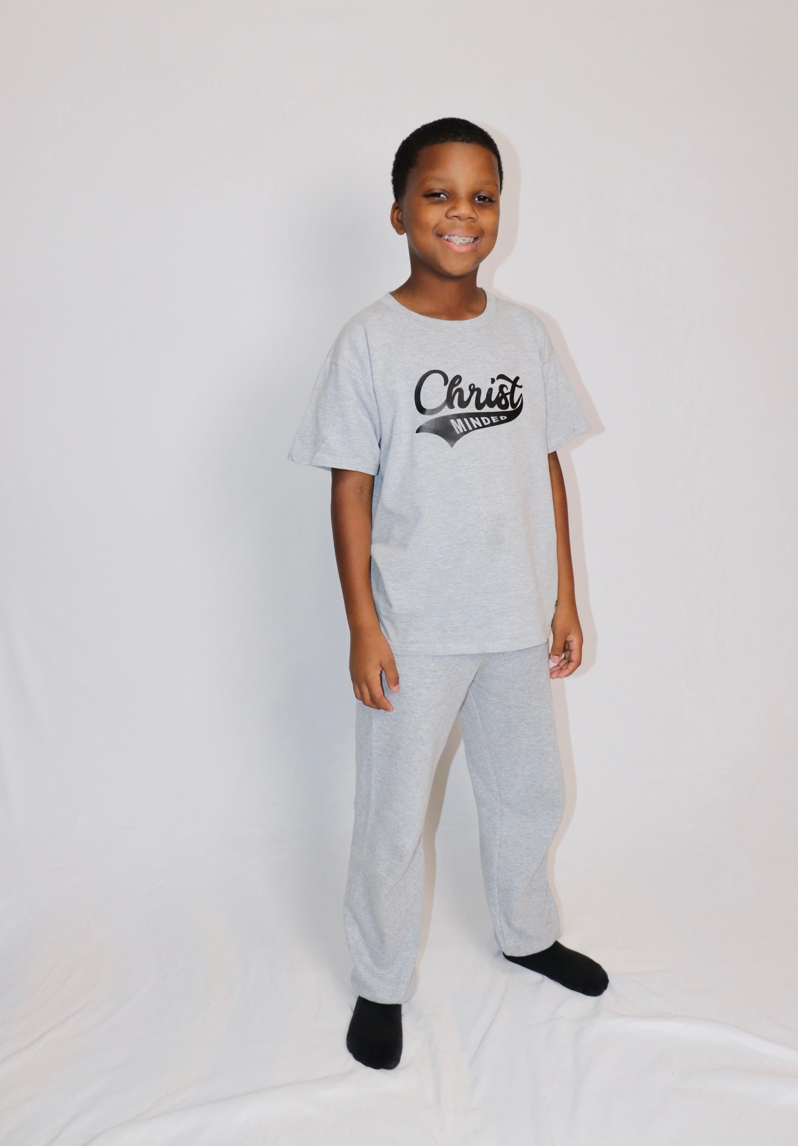 Smiling boy wearing a gray Christ Minded t-shirt and matching pants, representing a comfortable faith-based outfit for kids