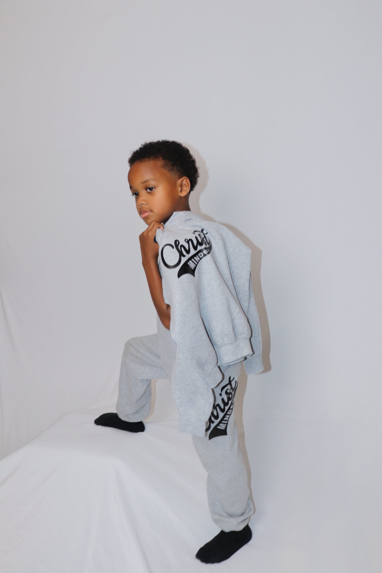 Boy posing in gray Christ Minded sweatpants holding matching sweatshirt over his shoulder