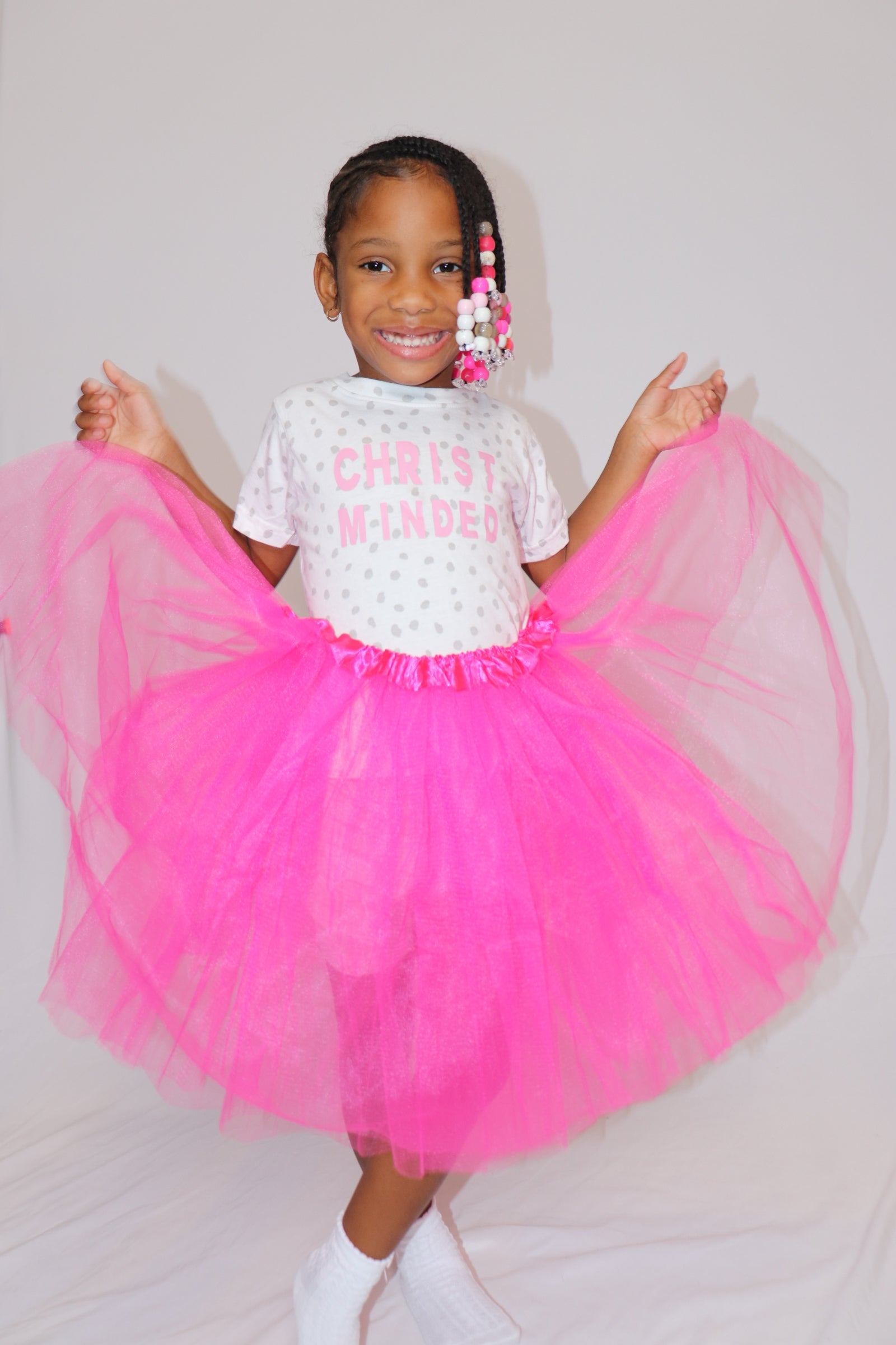 Young girl wearing a Christ Minded polka dot t-shirt with a bright pink tutu, smiling joyfully in a faith-based kids apparel photoshoot