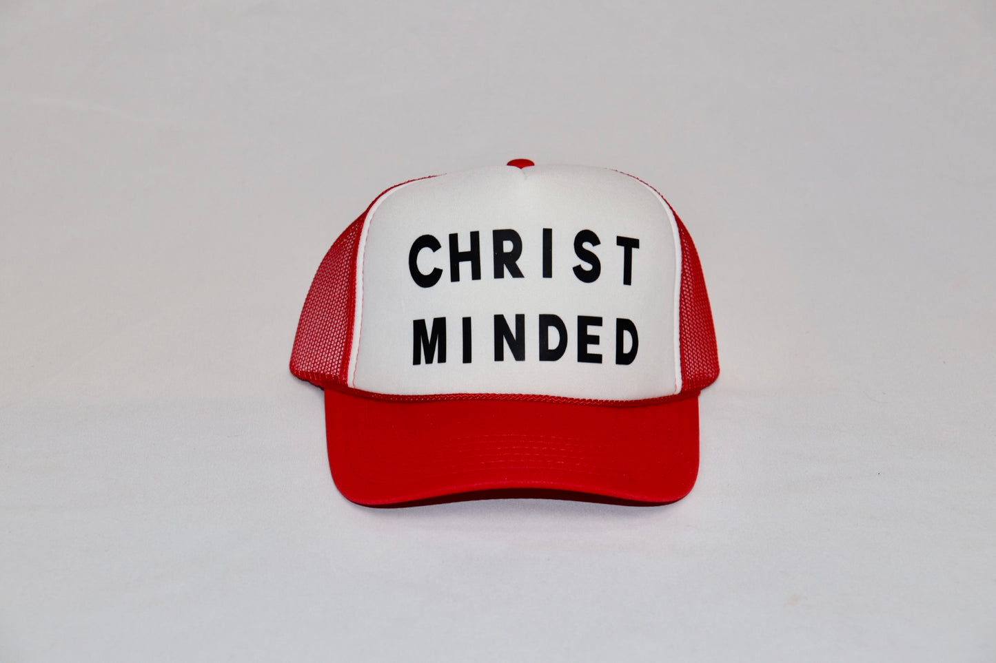 Red and white Christ Minded trucker hat with bold black lettering on front panel
