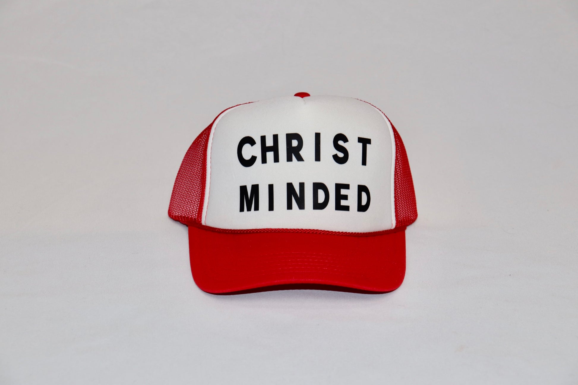 Red and white Christ Minded trucker hat with bold black lettering on front panel