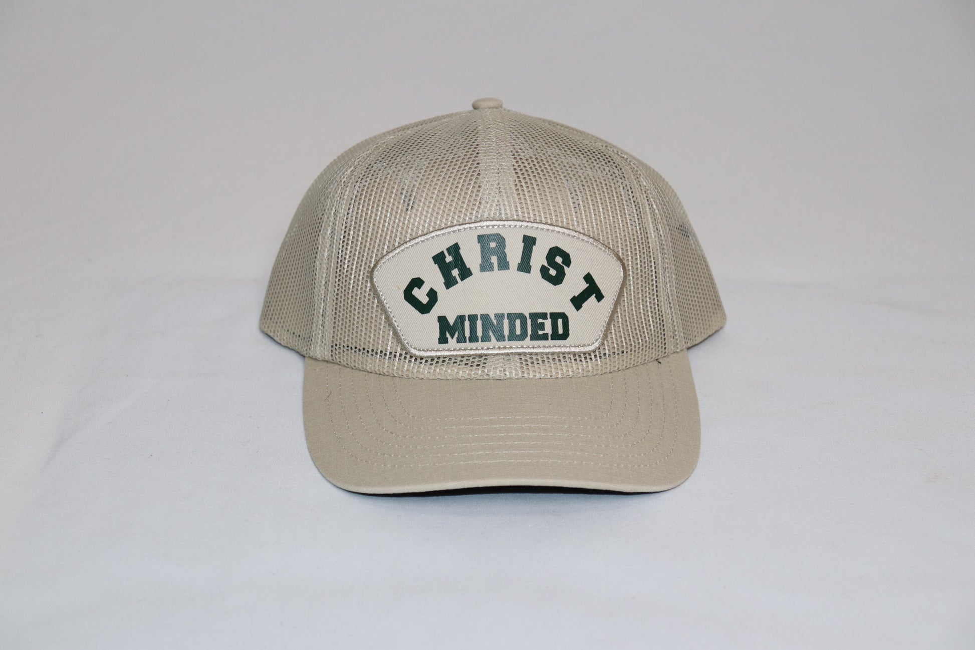 Christ Minded Sandstone Faith Cap with beige mesh and green embroidered patch reading “Christ Minded,” a vintage Christian trucker hat inspired by Philippians 2:5.